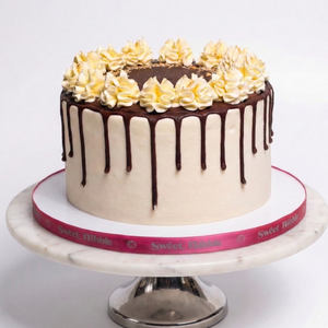 Cake with chocolate drizzle and yellow flowers on a white stand
